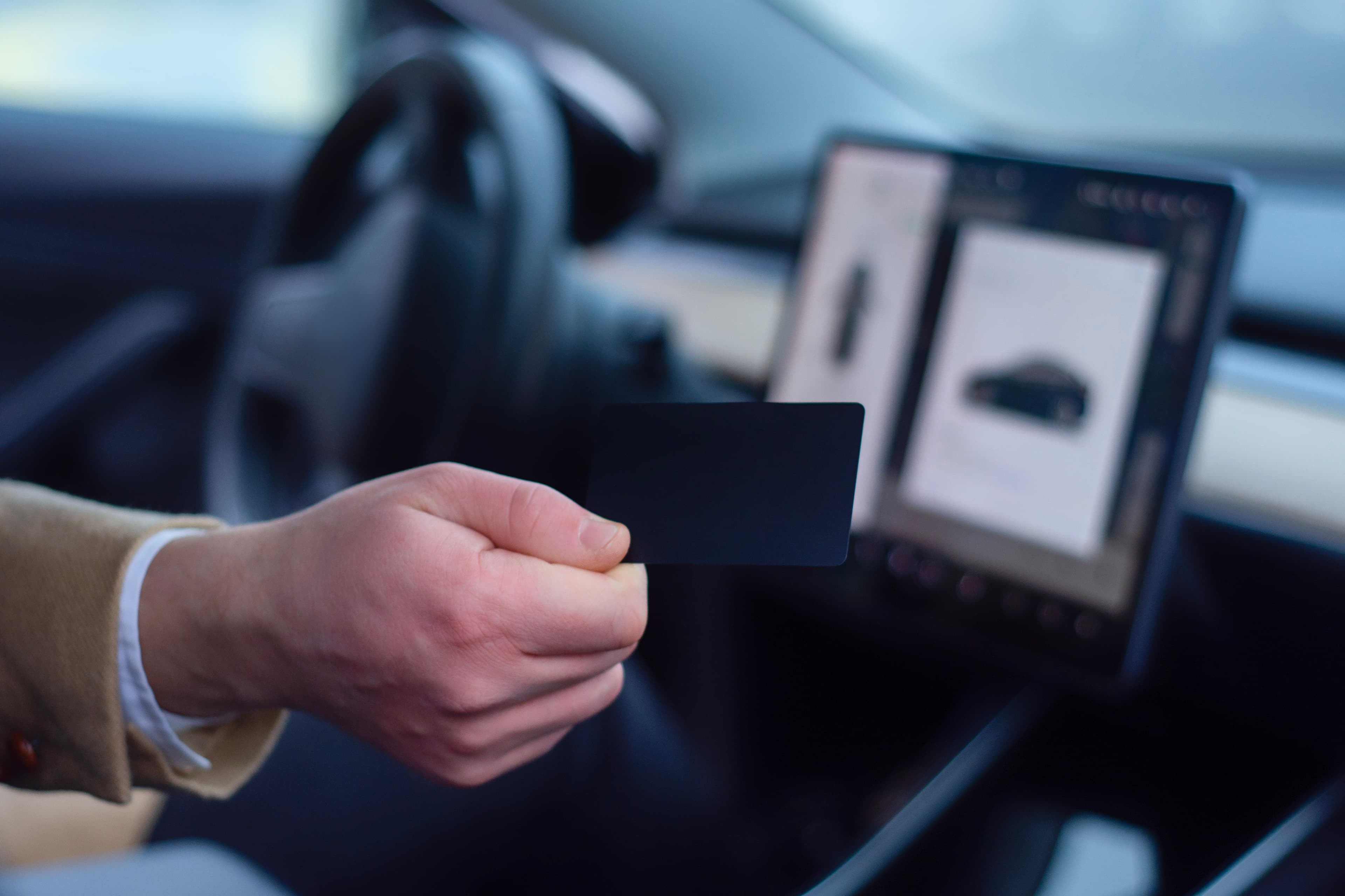 Driver holding an identification card in front of an in-vehicle display.
